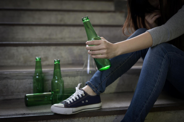 Młoda dziewczyna a prolemem alkoholowym siedzi na schodach i pije